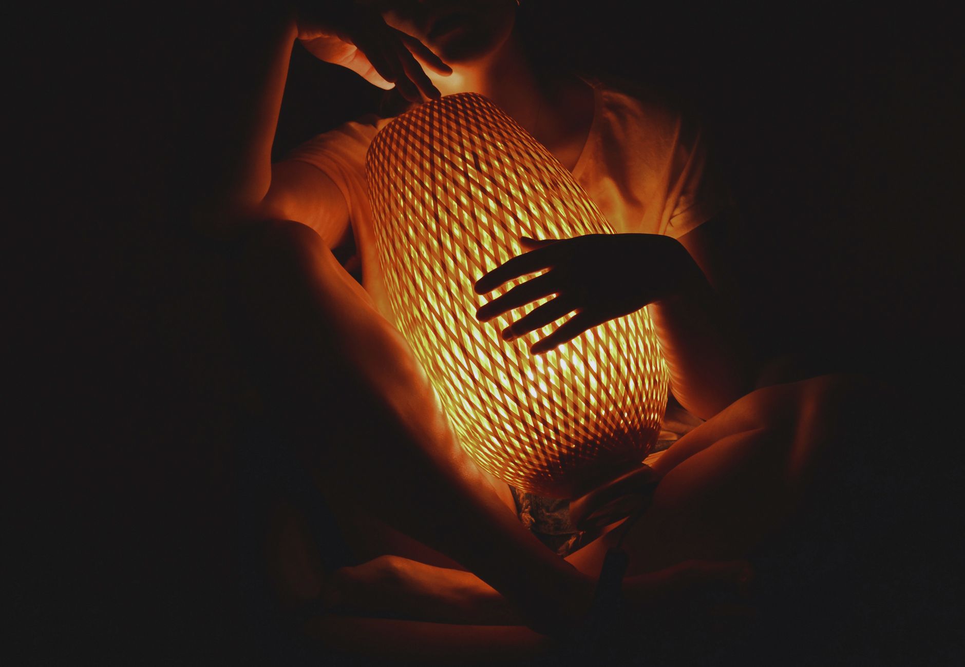 Uma mulher sentada sozinha em frente a um grande espelho, luz suave e quente de candeeiro, a olhar para o próprio reflexo com uma expressão calma, ambiente acolhedor de quarto, plano médio - Foto de Darya Grey_Owl no Unsplash