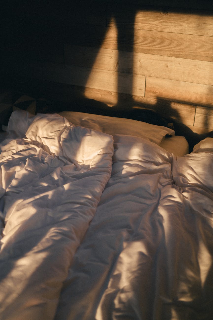 Close-up of someone's hands resting calmly on a white duvet in soft morning light