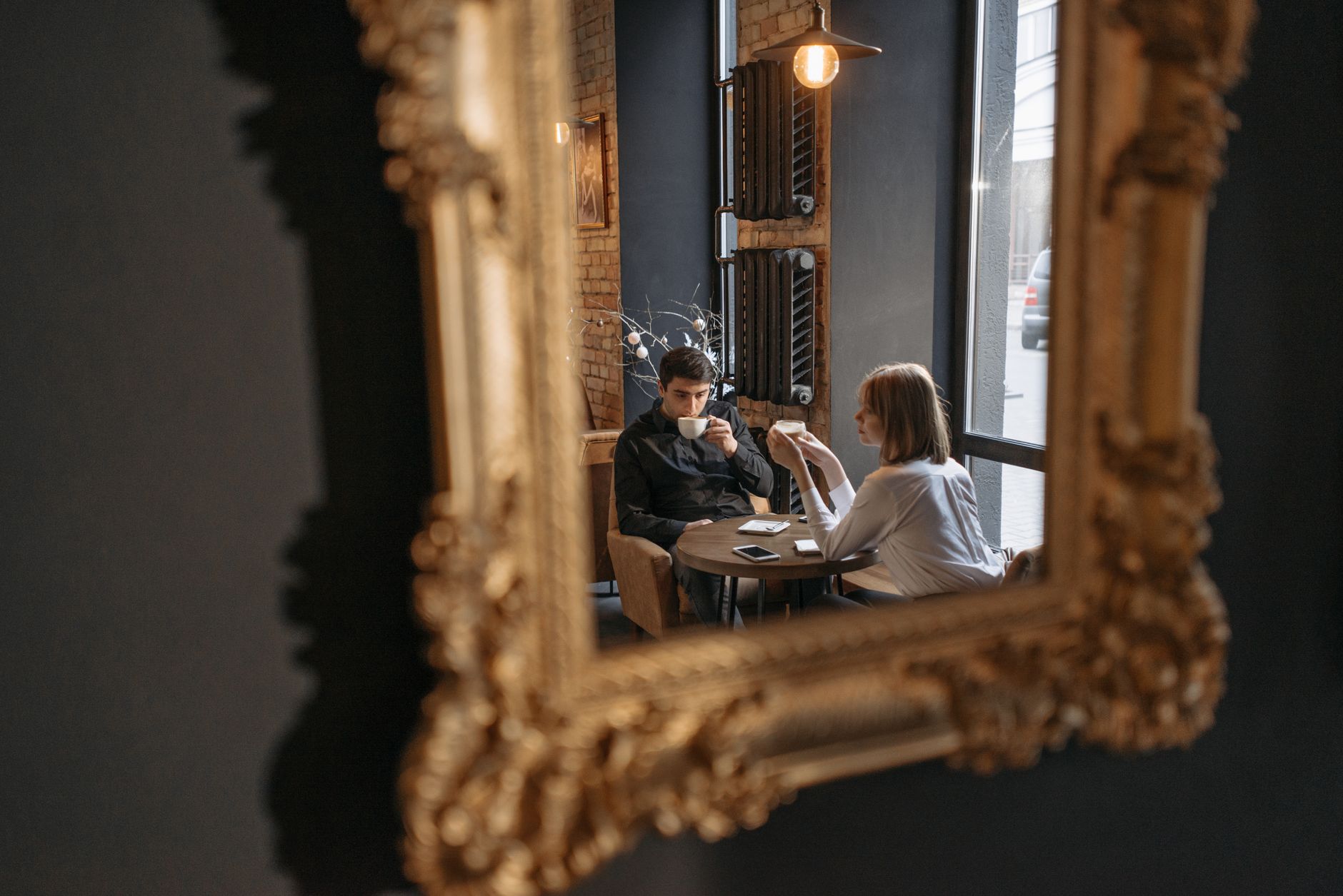 Duas pessoas sentadas frente a frente numa pequena mesa de café, uma a rir de olhos fechados, a outra inclinada para a frente a sorrir, iluminação interior quente, estilo documental espontâneo, bokeh suave ao fundo - Fotografia de Pavel Danilyuk no Unsplash