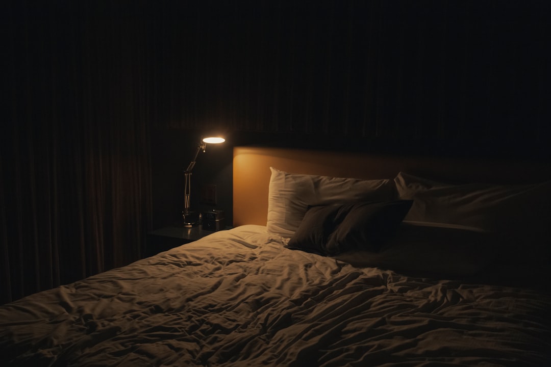 Portrait-format shot of a smiling person sitting cross-legged on a bed in cozy knitwear, holding a warm mug, soft indoor lamp light, relaxed and comfortable home setting, warm color tones - Photo by Jp Valery on Unsplash